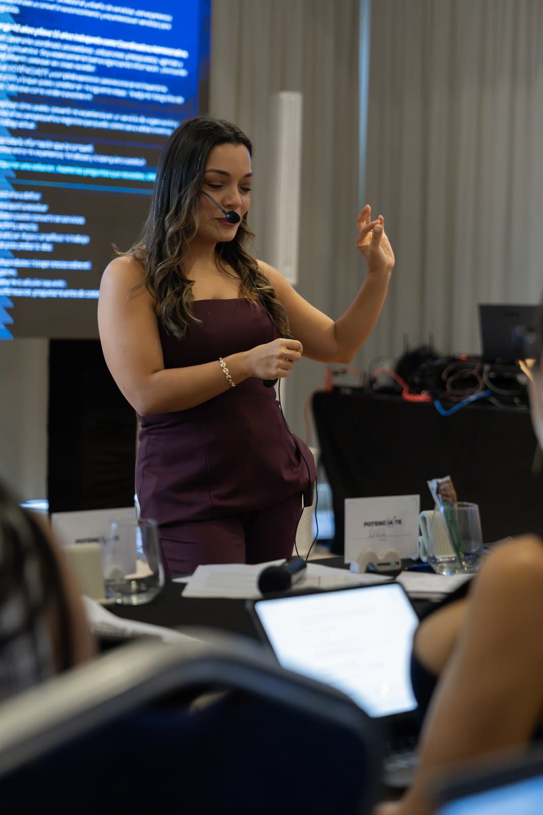 Anji Santiago facilitando un taller con micrófono de diadema frente a una pantalla